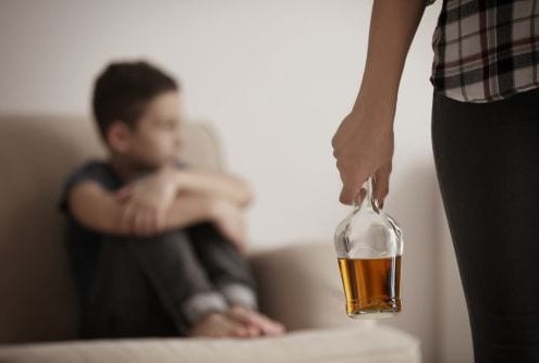 Woman holding bottle of alcohol with little boy sitting on the couch in the background