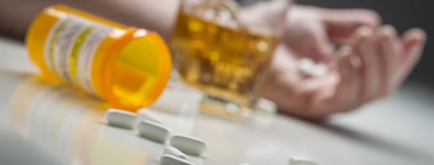 Deadly Drug Combinations- spilt pills on a table with a glass of alcohol